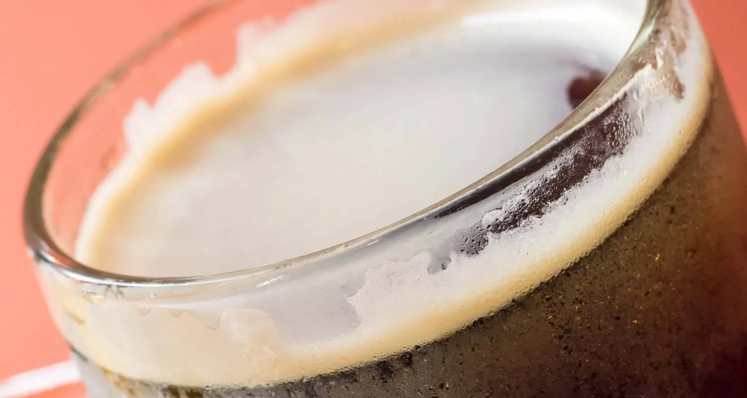 Glas mit dunklem Root Beer und dichter Schaumkrone auf hellem Untergrund