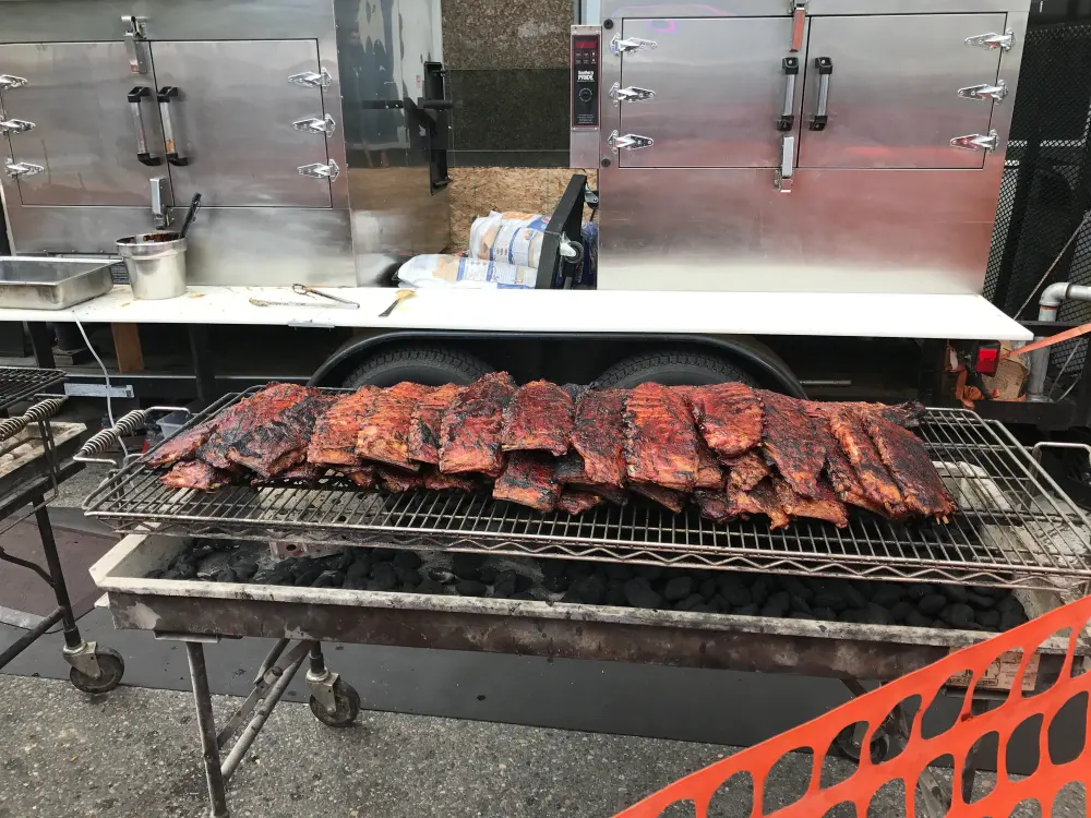 Lange Reihe Spareribs auf dem Rost eines Trommelgrills, dunkel glasiert